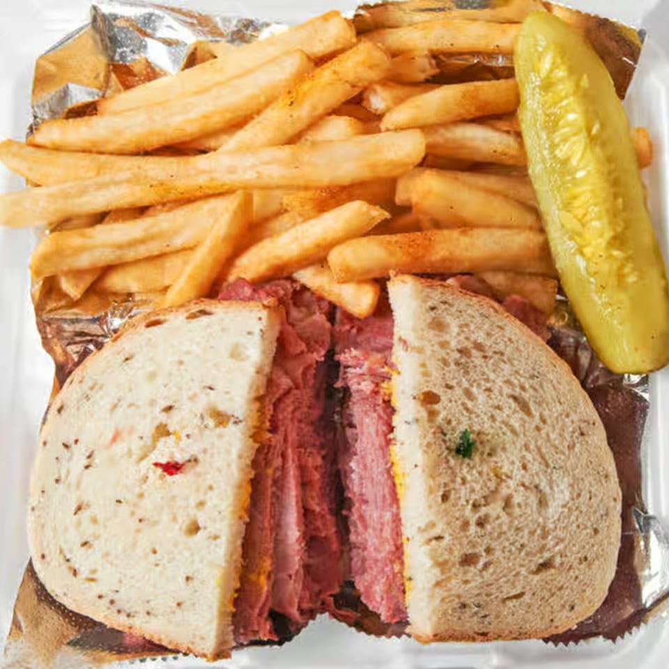 Dale's Deli pastrami sandwich cut in half, with a side of fries and a pickle spear.