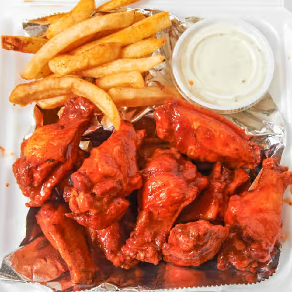 Dale's Deli hot wings and french fries with a side of ranch dressing in a takeout container.