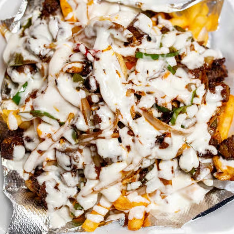 Close-up of Dale's Deli fries topped with melted cheese, meat, onions, and green herbs in foil.